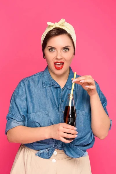 Surprised size plus pin up woman holding glass bottle with drinking straw and looking at camera isolated on pink — Stock Photo