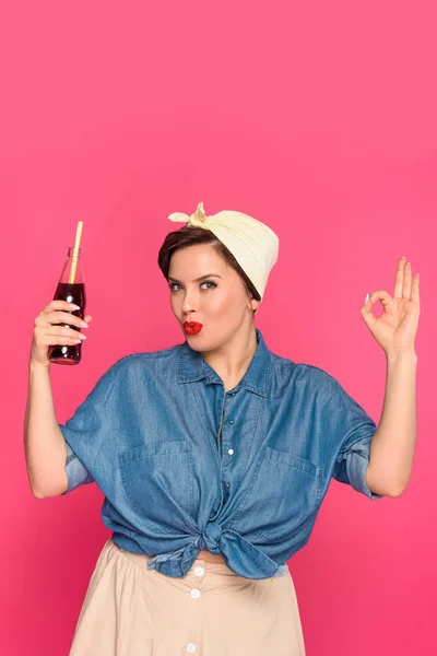 Bela pin up mulher segurando garrafa de vidro com palha bebendo e mostrando sinal ok isolado em rosa — Fotografia de Stock