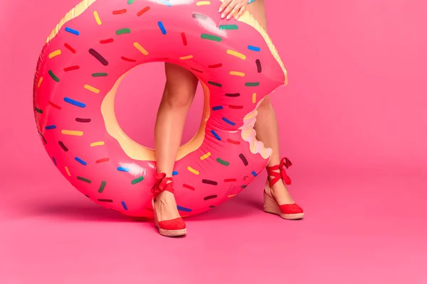 Tiro recortado de chica en calzado rojo sosteniendo anillo inflable aislado en rosa - foto de stock