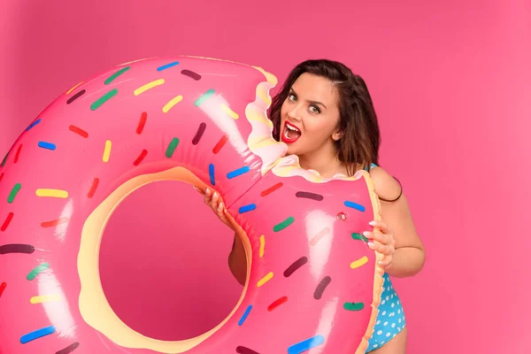 Jovem morena em roupa de banho segurando anel inflável e olhando para a câmera isolada em rosa — Fotografia de Stock