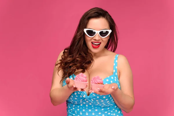 Hermosa mujer sonriente en traje de baño y gafas de sol con deliciosos cupcakes aislados en rosa - foto de stock