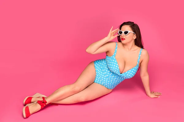 Повний вигляд сексуального розміру плюс жінка в купальнику і сонцезахисних окулярах, що відпочивають ізольовані на рожевому — стокове фото