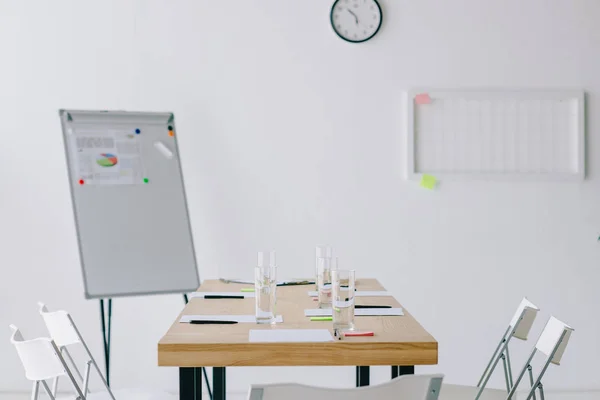 Mise au point sélective du tableau blanc avec graphique, verres d'eau et documents sur le lieu de travail au bureau — Photo de stock