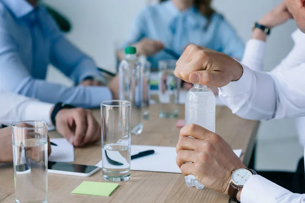 Обрізаний знімок бізнесмена, що відкриває пляшку води з колегами на робочому місці поруч в офісі — стокове фото