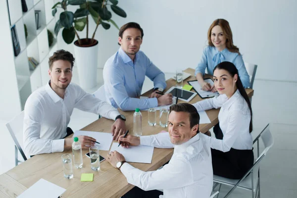 Vista de ángulo alto de los colegas de negocios sonrientes en el lugar de trabajo con papeles en la oficina — Stock Photo