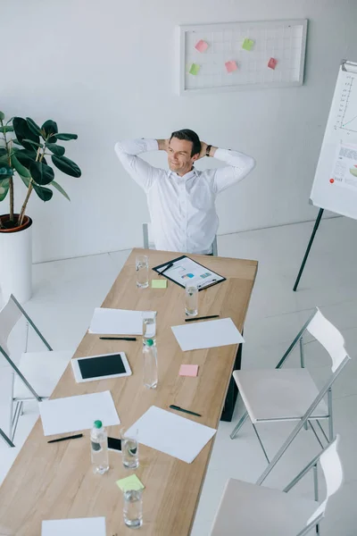 Vista ad alto angolo di uomo d'affari sorridente in abbigliamento formale seduto da solo sul posto di lavoro in ufficio — Foto stock