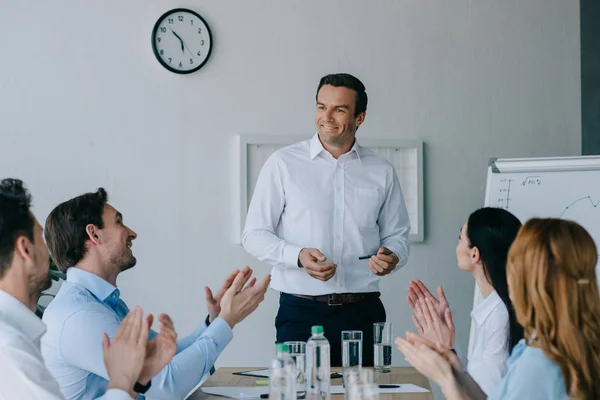 Бізнес-партнери аплодують усміхненому наставнику під час бізнес-тренінгу в офісі — стокове фото