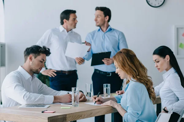 Compañeros de trabajo con papeles que tienen formación empresarial en la oficina - foto de stock