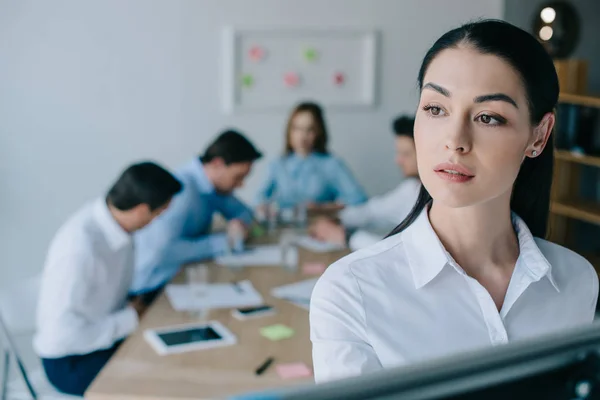 Enfoque selectivo de la empresaria pensativa y colegas detrás en el lugar de trabajo en la oficina - foto de stock