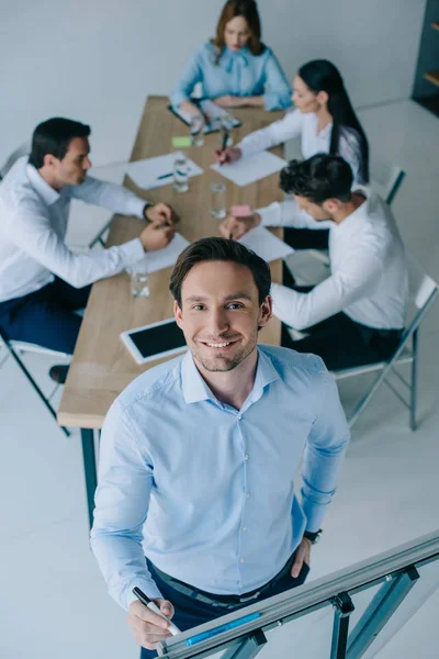 Selective focus of smiling businessman at white board and coworkers at workplace in office — Stock Photo