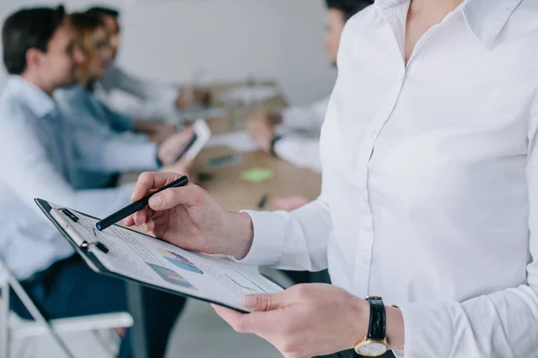 Partial view of businesswoman with notepad and colleagues at workplace in office — Stock Photo