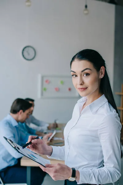 Enfoque selectivo de la mujer de negocios con bloc de notas y colegas en el lugar de trabajo en la oficina - foto de stock