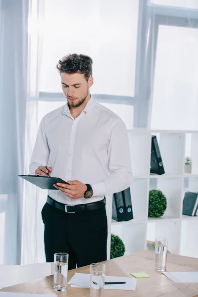 Porträt eines Geschäftsmannes in offizieller Kleidung, der Notizen im Notizblock im Büro macht — Stockfoto