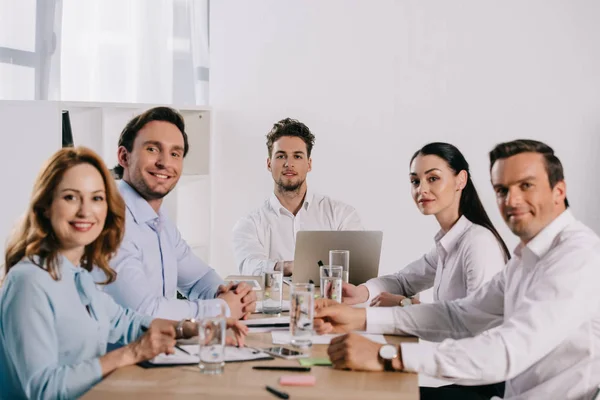 Enfoque selectivo de los colegas de negocios sonrientes en el lugar de trabajo con documentos en la oficina - foto de stock