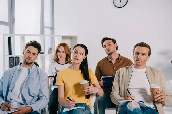 Portrait of focused businessmen and businesswomen in casual clothing with notebooks on business training in office — Stock Photo