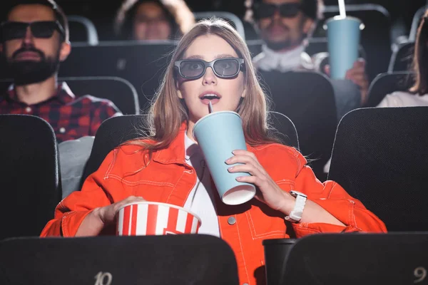 Selektiver Fokus einer schockierten Frau in 3D-Gläsern, die Limo trinkt und Film im Kino anschaut — Stockfoto