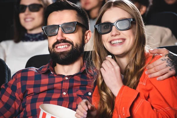 Красивий хлопець обіймає усміхнену дівчину в 3d окулярах і дивиться фільм в кіно — стокове фото