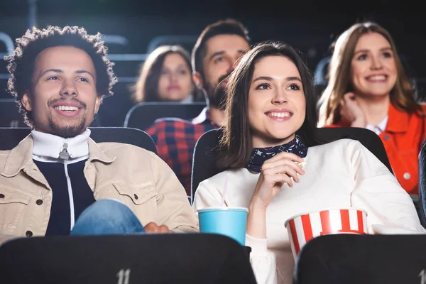 Selective focus of multiethnic friends smiling and watching movie in cinema — Stock Photo