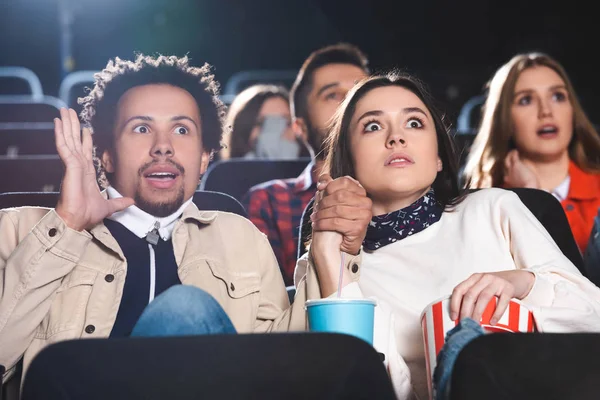 Selektiver Fokus multiethnischer und schockierter Freunde, die sich Händchen halten und Filme im Kino ansehen — Stockfoto