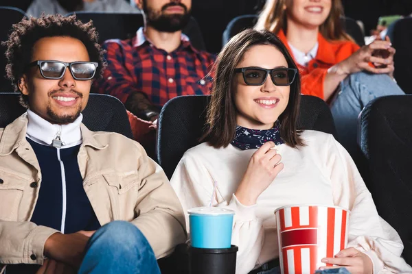 Селективное внимание многонациональных друзей в 3D очках, улыбающихся и смотрящих кино в кино — стоковое фото