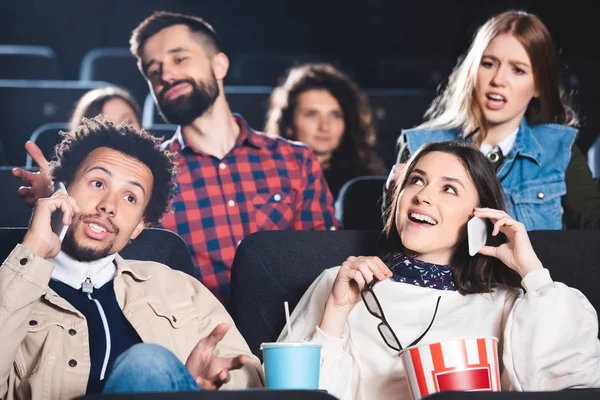 Enfoque selectivo de amigos multiétnicos tomando el teléfono inteligente y sonriendo en el cine - foto de stock