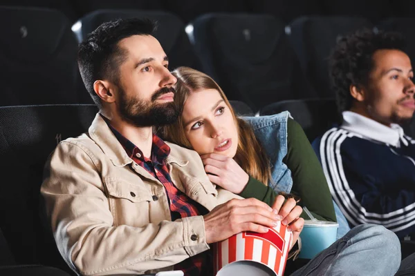 Selective focus of scared woman lying on shoulder and watching movie with multicultural friends in cinema — Stock Photo