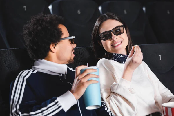 Multicultural friends in 3d glasses looking at each other and smiling in cinema — Stock Photo