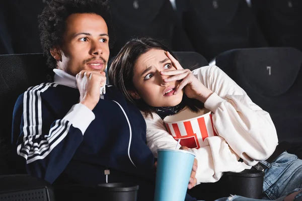 Amigos multiculturales asustados con palomitas de maíz viendo películas en el cine - foto de stock