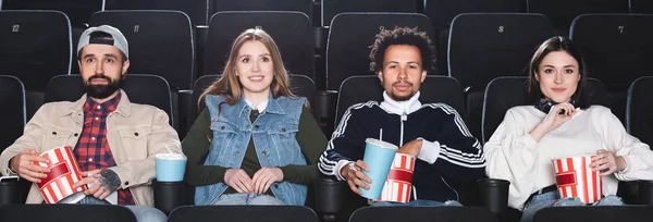 Panoramica di amici multiculturali che sorridono e guardano film al cinema — Foto stock