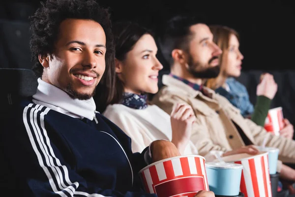 Selective focus of african american man with friends looking at camera in cinema — Stock Photo
