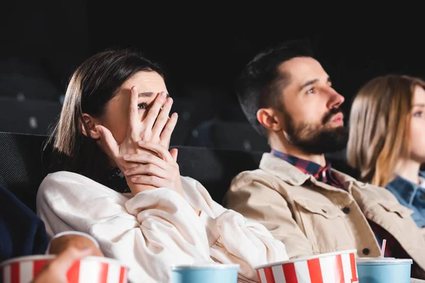 Messa a fuoco selettiva della donna spaventata oscurando il viso e guardando film con gli amici nel cinema — Foto stock