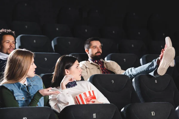 Multicultural friends with popcorn looking at ill-mannered man in cinema — Stock Photo