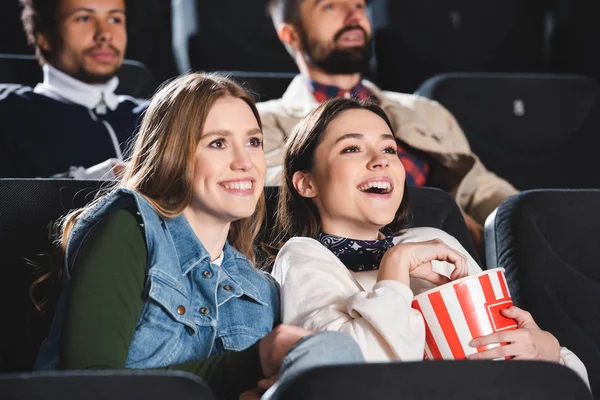 Enfoque selectivo de amigos sonrientes con palomitas de maíz viendo películas en el cine - foto de stock