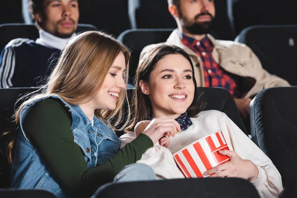 Selective focus of smiling friends with popcorn watching movie in cinema — Stock Photo