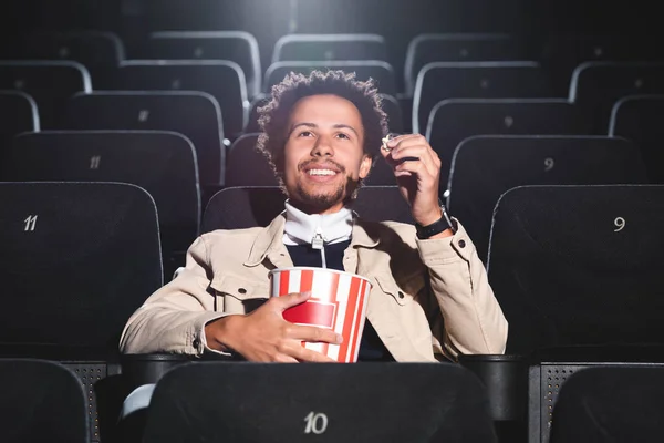 Souriant homme afro-américain tenant du pop-corn et regardant un film au cinéma — Photo de stock