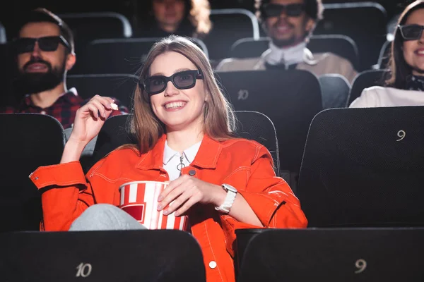 Selective focus of smiling woman in 3d glasses with popcorn watching movie in cinema — Stock Photo