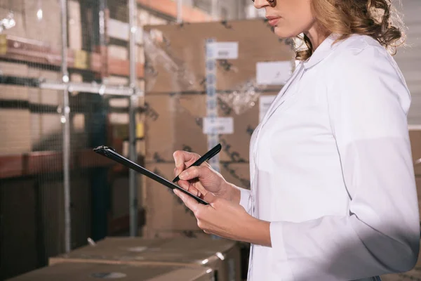 Partial view of storekeeper writing on clipboard in warehouse — Stock Photo