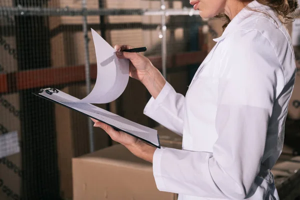 Cropped view of storekeeper holding clipboard with documents in warehouse — Stock Photo