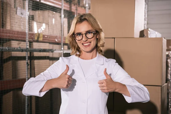 Cheerful storekeeper in glasses showing thumbs up and looking at camera — Stock Photo