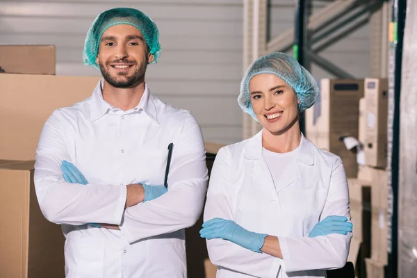 Two cheerful storekeepers standing with crossed arms while smiling at camera — Stock Photo