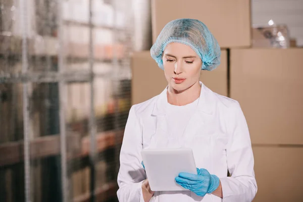 Magasinier concentré dans hairnet en utilisant la tablette numérique dans l'entrepôt — Photo de stock