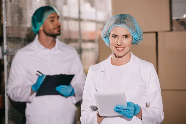 Selektiver Fokus eines attraktiven Ladenbesitzers, der ein digitales Tablet in der Nähe eines Kollegen hält, der auf Klemmbrett schreibt — Stockfoto