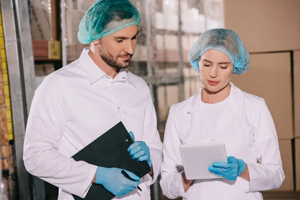 Schöner Ladenbesitzer hält Klemmbrett in der Nähe attraktiver Kollege mit digitalem Tablet — Stockfoto