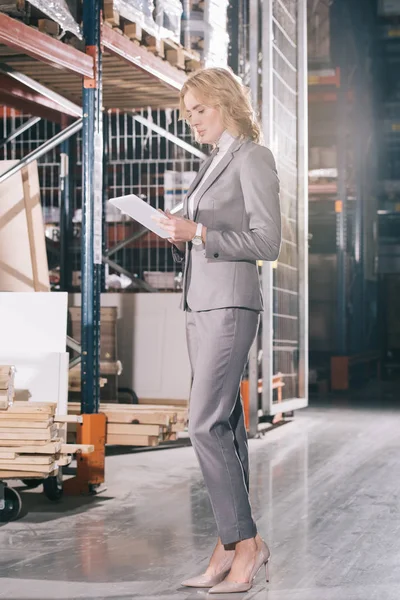 Fokussierte Geschäftsfrau benutzt Laptop, während sie in der Nähe von Baumaterialien in einer Lagerhalle steht — Stockfoto