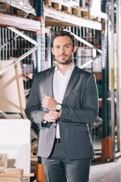 Handsome businessman in formal wear smiling at camera while standing in warehouse — Stock Photo