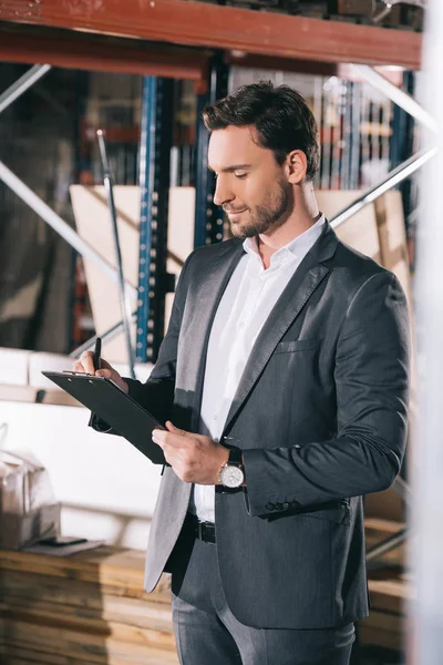 Concentrated businessman writing on clipboard in warehouse — Stock Photo