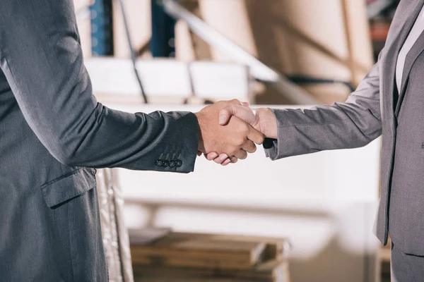 Cropped view of businesspeople shaking hands in warehouse — Stock Photo