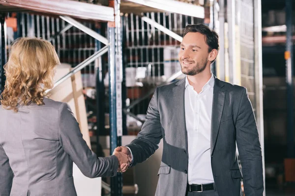 Homem de negócios sorridente apertando as mãos com empresária em armazém — Fotografia de Stock