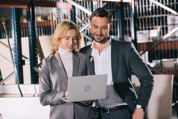 Smiling businesspeople looking at laptop while standing in warehouse — Stock Photo