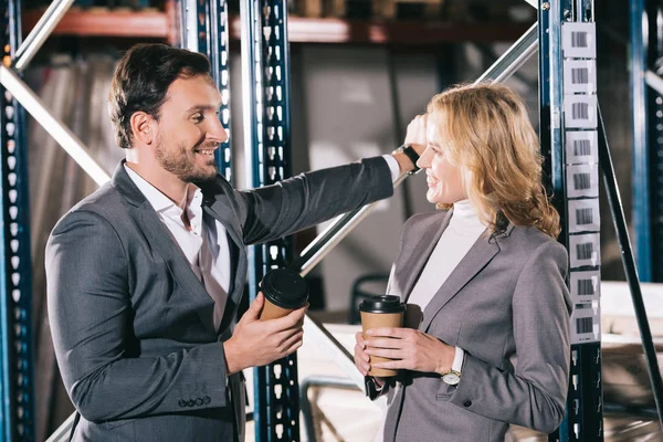 Zwei lächelnde Geschäftsleute unterhalten sich im Lager, während sie Einwegbecher in der Hand halten — Stockfoto